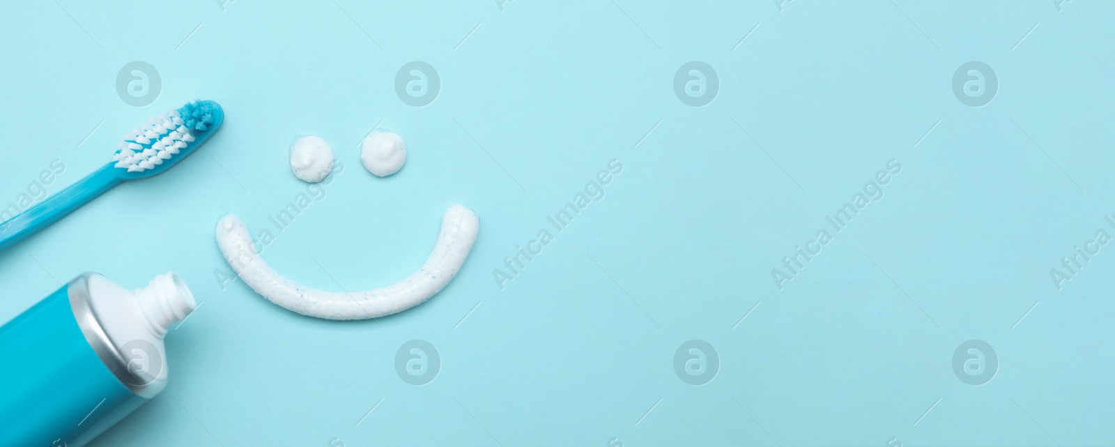 Image of Smiling face made of toothpaste, brush and tube on light blue background, flat lay with space for text. Banner design