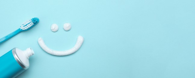 Image of Smiling face made of toothpaste, brush and tube on light blue background, flat lay with space for text. Banner design