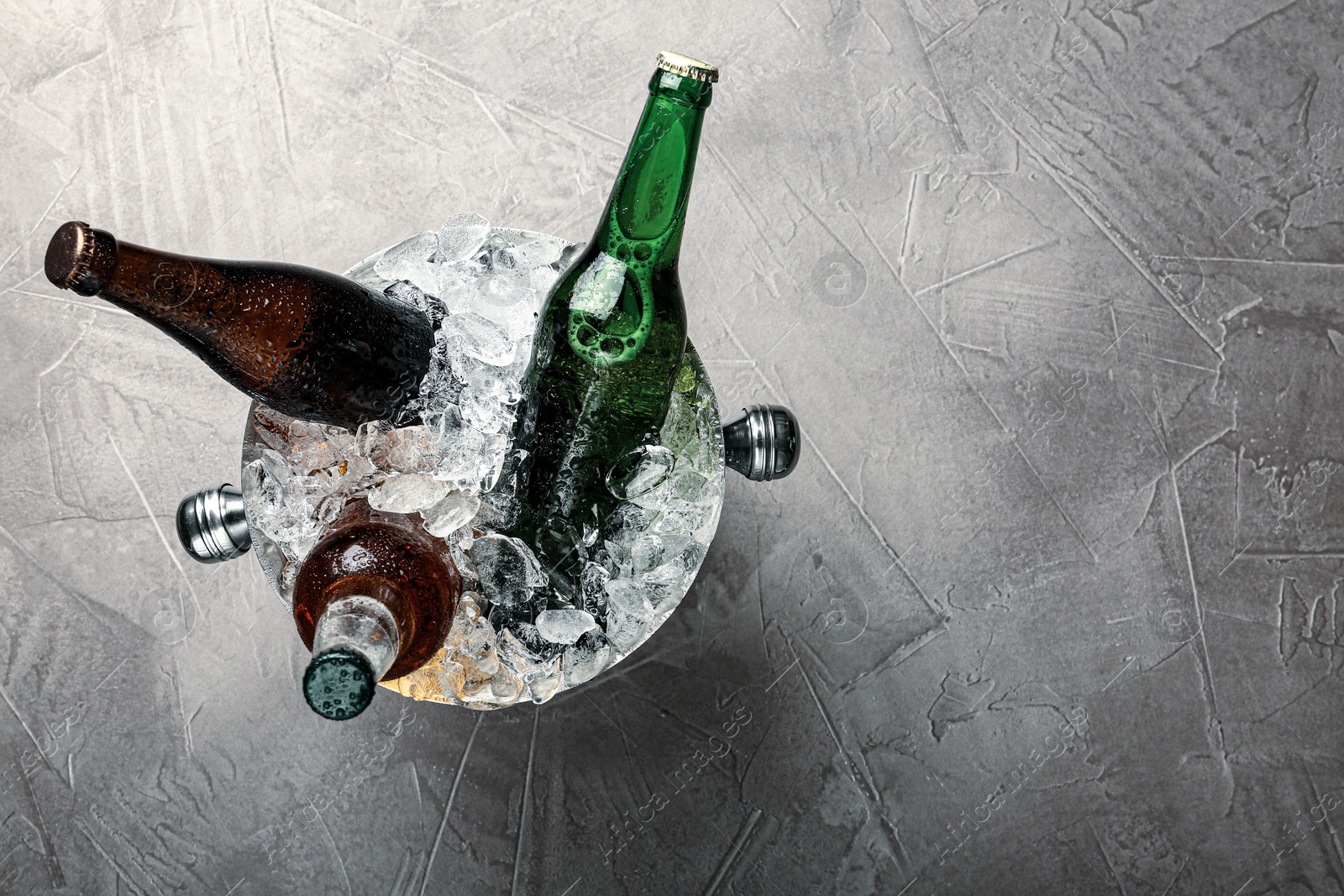 Photo of Beer in metal bucket with ice on grey table, top view. Space for text