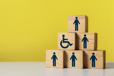 Image of Inclusive workplace culture. Pyramid of wooden cubes with human icons and one with international symbol of access on yellow background