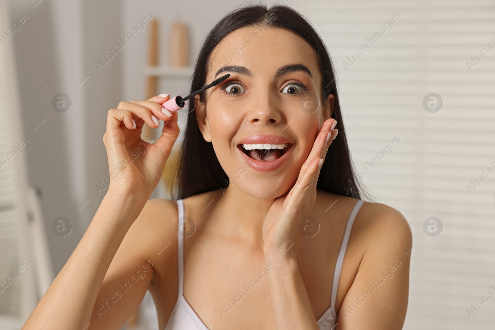 Photo of Beautiful young woman applying mascara indoors, closeup