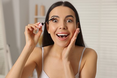 Beautiful young woman applying mascara indoors, closeup