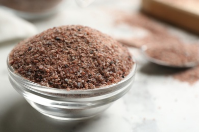 Photo of Ground black salt in glass bowl on white table, closeup. Space for text