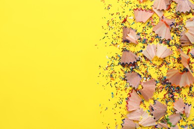 Photo of Many colorful pencil shavings on yellow background, flat lay. Space for text