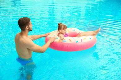 Father and daughter with inflatable ring in swimming pool