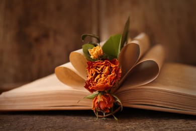 Photo of Open book with folded pages and beautiful dried flowers on wooden table, closeup
