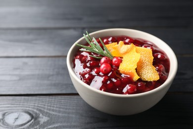 Photo of Fresh cranberry sauce, rosemary and orange peel in bowl on black wooden table, closeup. Space for text