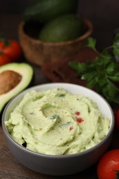 Photo of Bowl of delicious guacamole and ingredients on wooden table, closeup