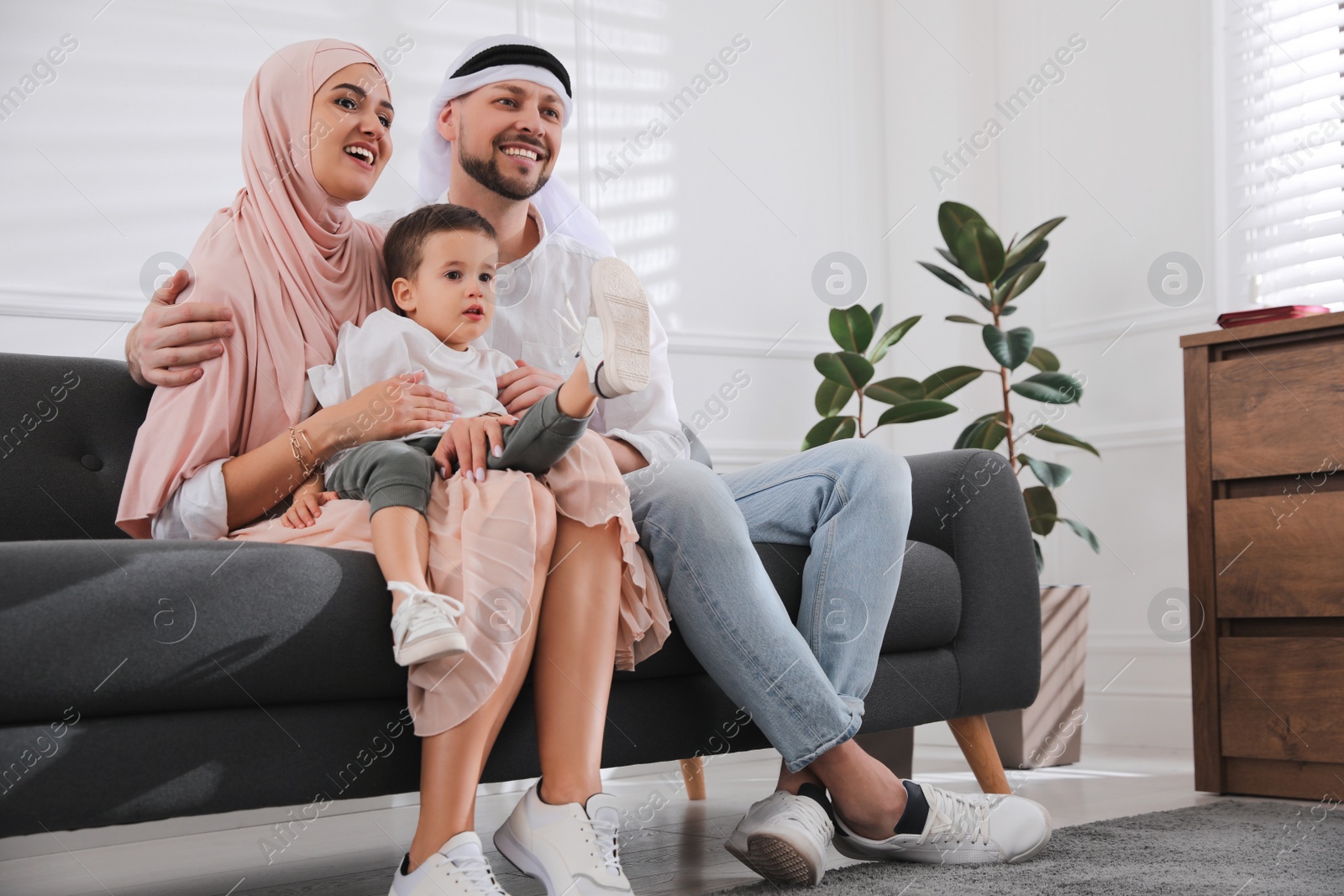 Photo of Happy Muslim family spending time together on sofa at home, space for text