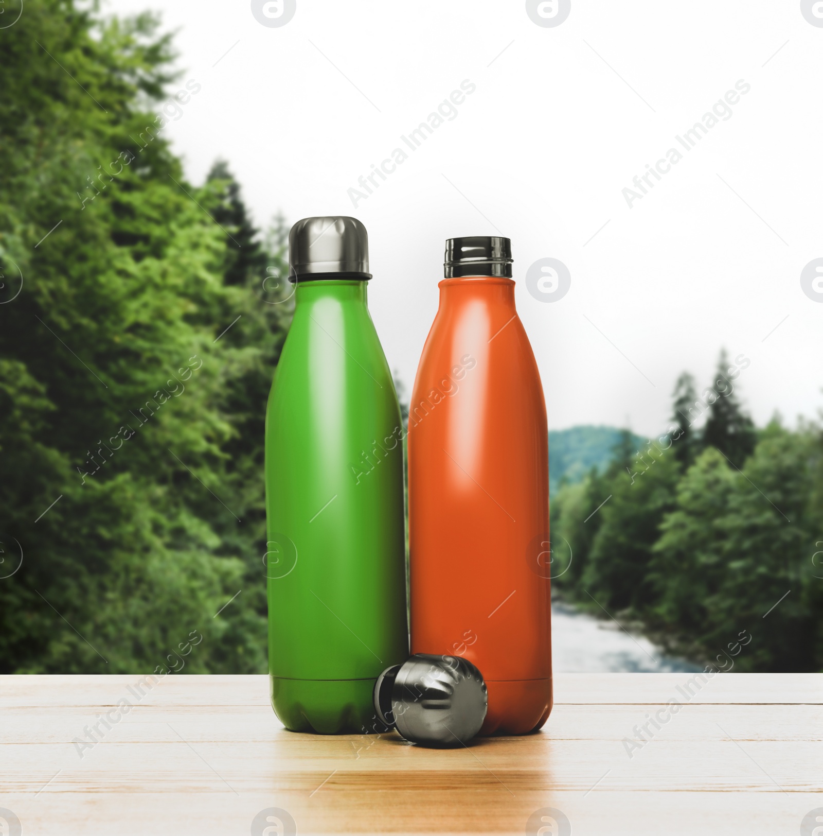 Image of Green and orange thermos bottles on wooden table against blurred mountain landscape