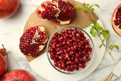 Photo of Ripe juicy pomegranate grains and green leaves on white marble table, flat lay