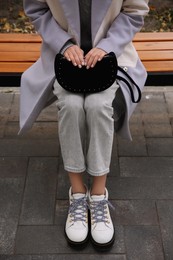 Stylish woman with trendy black baguette bag on bench outdoors, closeup