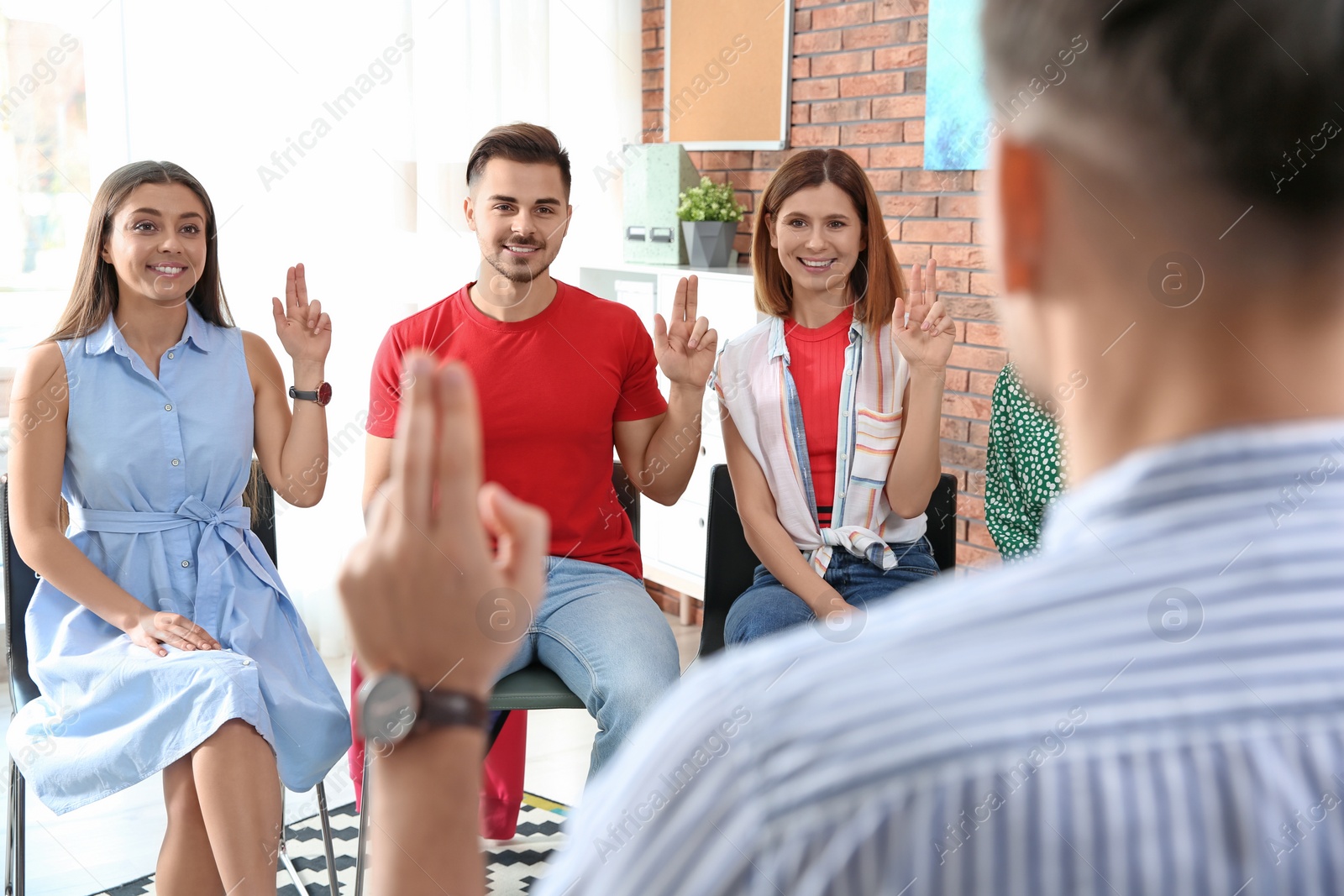 Photo of Group of young people learning sign language with teacher indoors