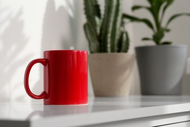 Photo of Red ceramic mug on white table indoors. Mockup for design