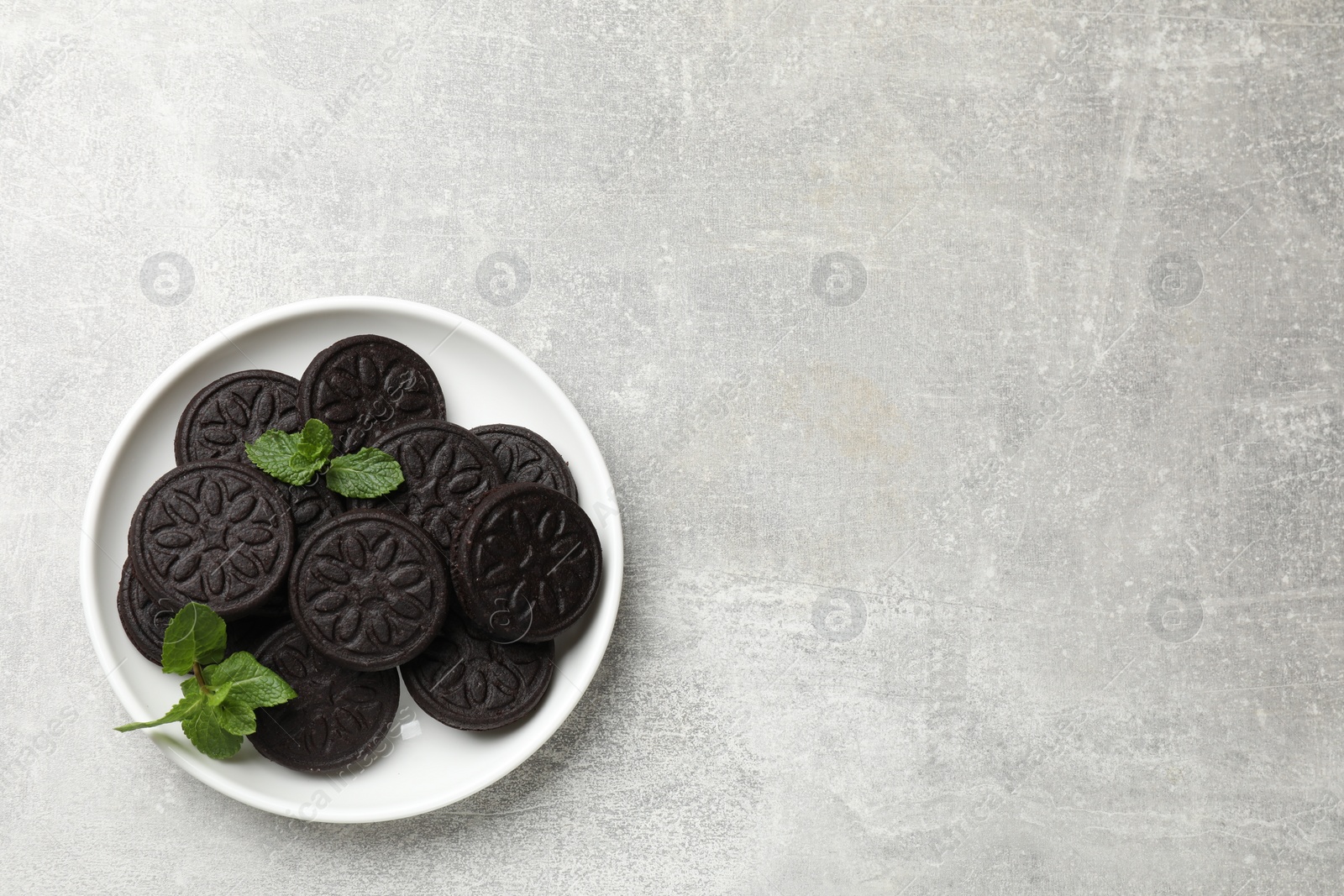 Photo of Plate with tasty sandwich cookies and mint on grey textured table, top view. Space for text