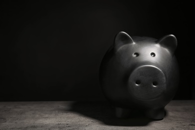 Black piggy bank on table against dark background with space for text. Poverty concept