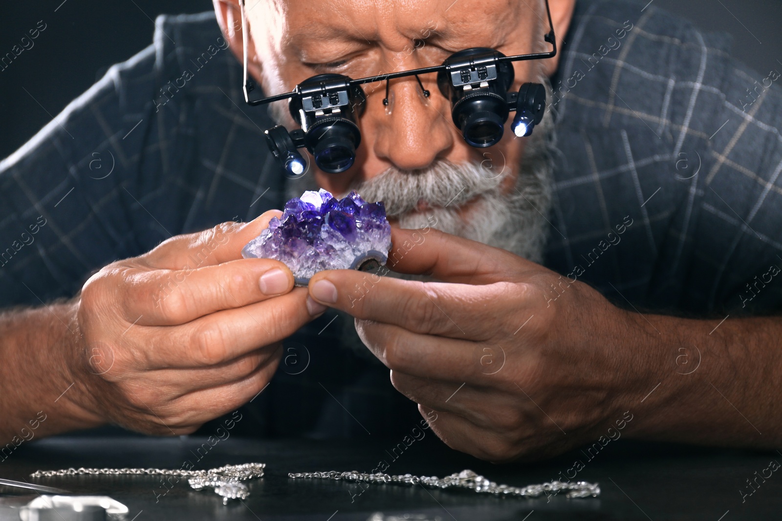Photo of Male jeweler evaluating amethyst in workshop, closeup view