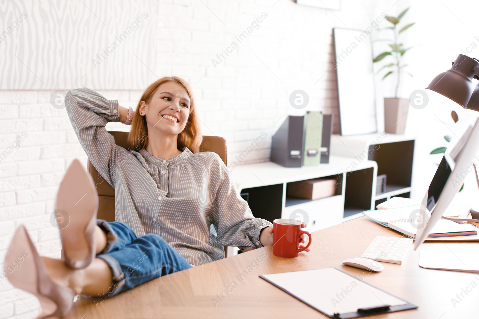 Photo of Young woman with cup of drink relaxing at table in office during break