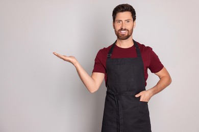 Professional hairdresser wearing apron and showing something on light grey background, space for text