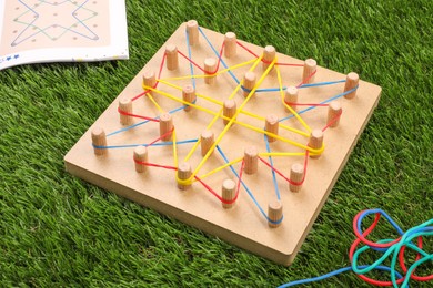 Photo of Wooden geoboard with rubber bands on artificial grass, closeup. Educational toy for motor skills development