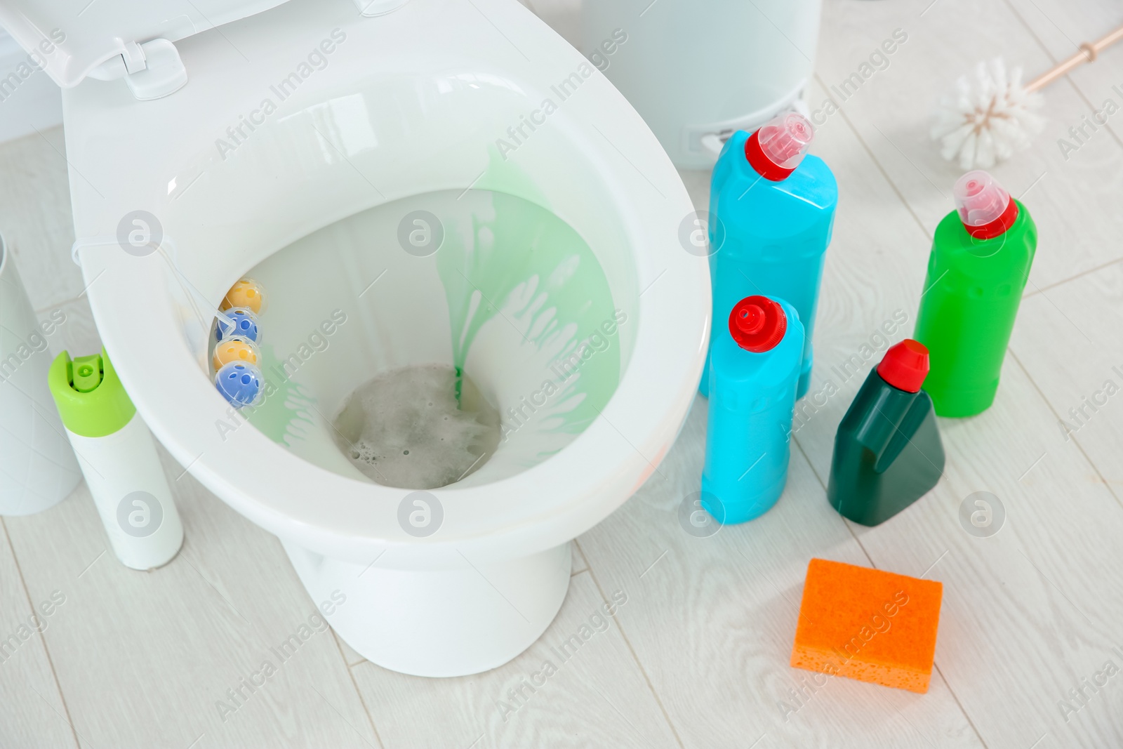 Photo of Ceramic toilet bowl, bottles of detergent and cleaning supplies in modern bathroom