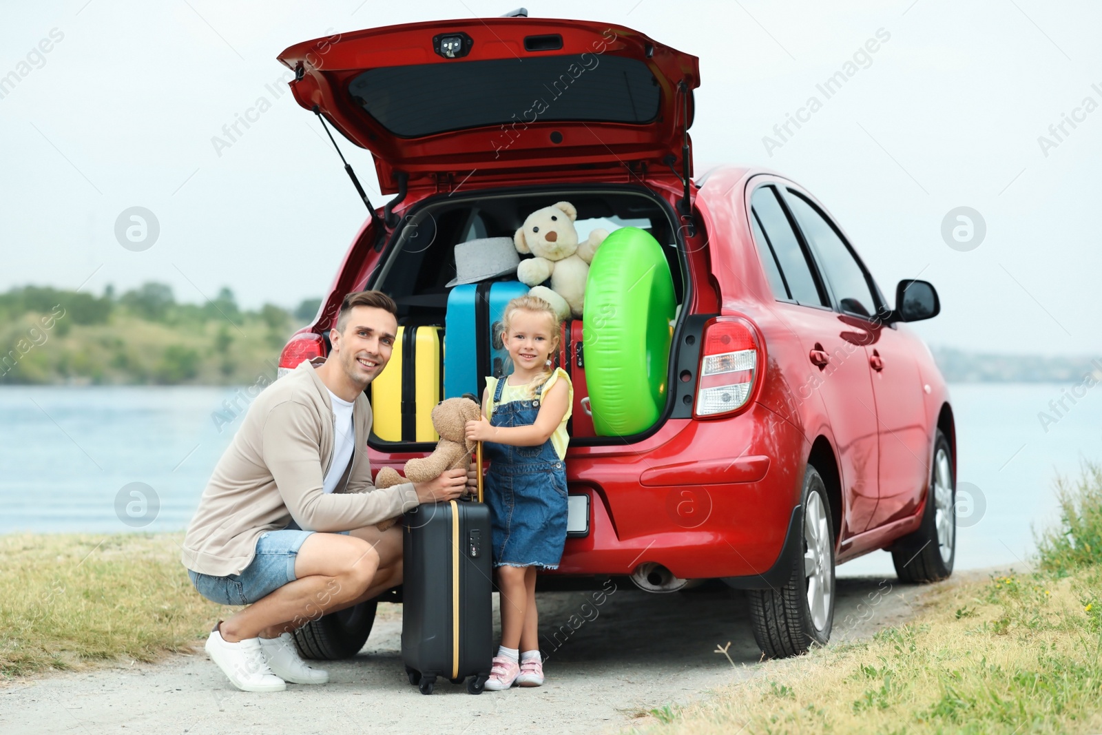 Photo of Father and daughter near car trunk with suitcases on riverside