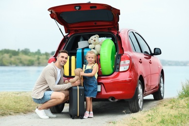 Photo of Father and daughter near car trunk with suitcases on riverside