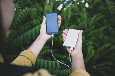 Woman charging smartphone with power bank in forest, closeup