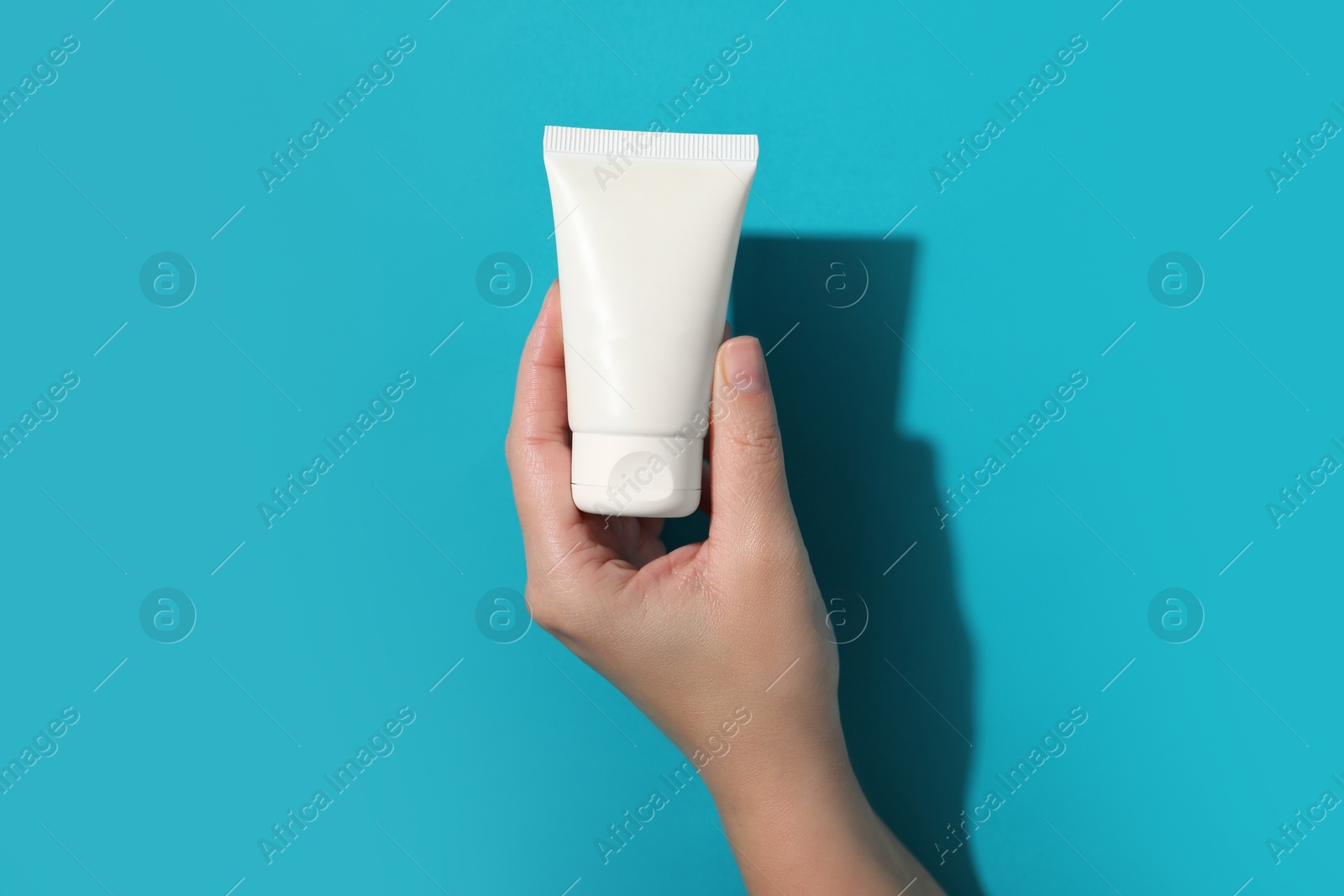 Photo of Woman with tube of hand cream on light blue background, top view