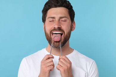 Photo of Happy man brushing his tongue with cleaner on light blue background