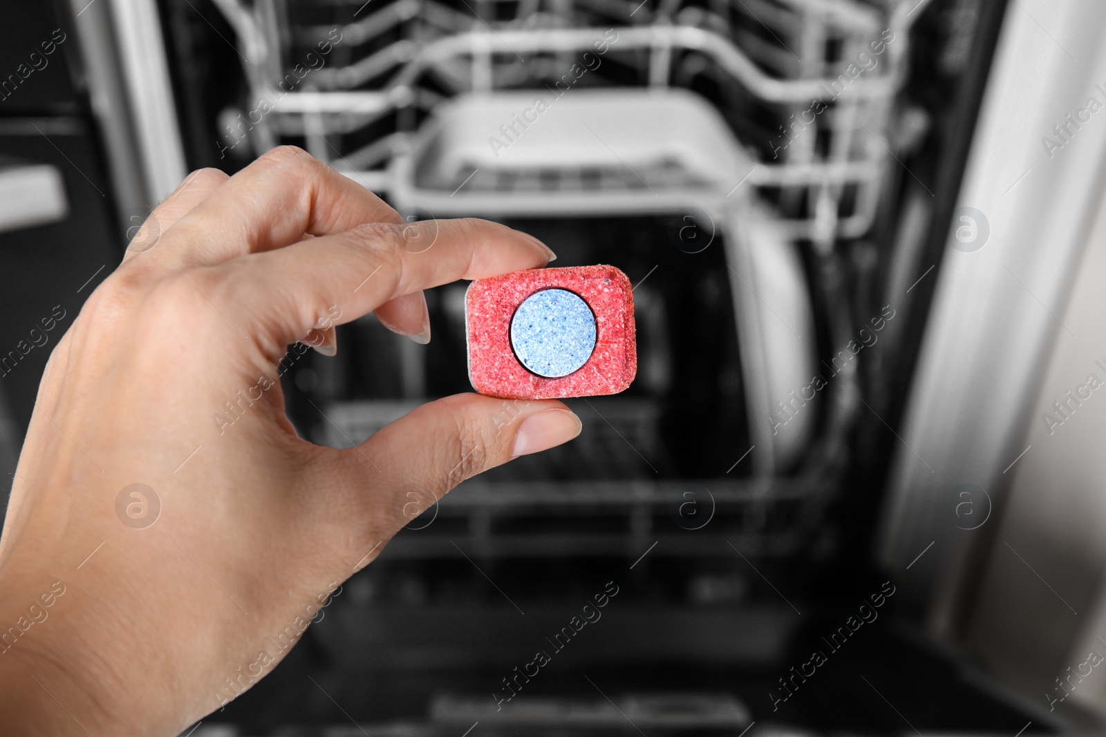 Photo of Woman putting detergent tablet into open dishwasher in kitchen, closeup