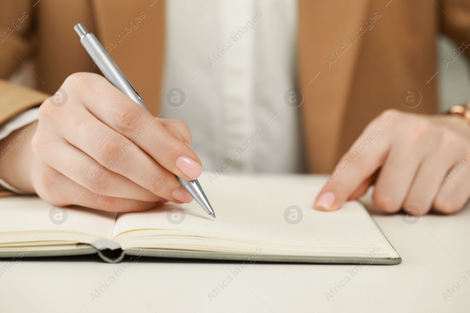 Photo of Woman writing in notebook at white table, closeup