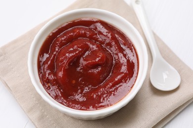 Organic ketchup in bowl and spoon on white table, closeup. Tomato sauce