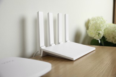 Photo of New modern Wi-Fi router on wooden table near white wall