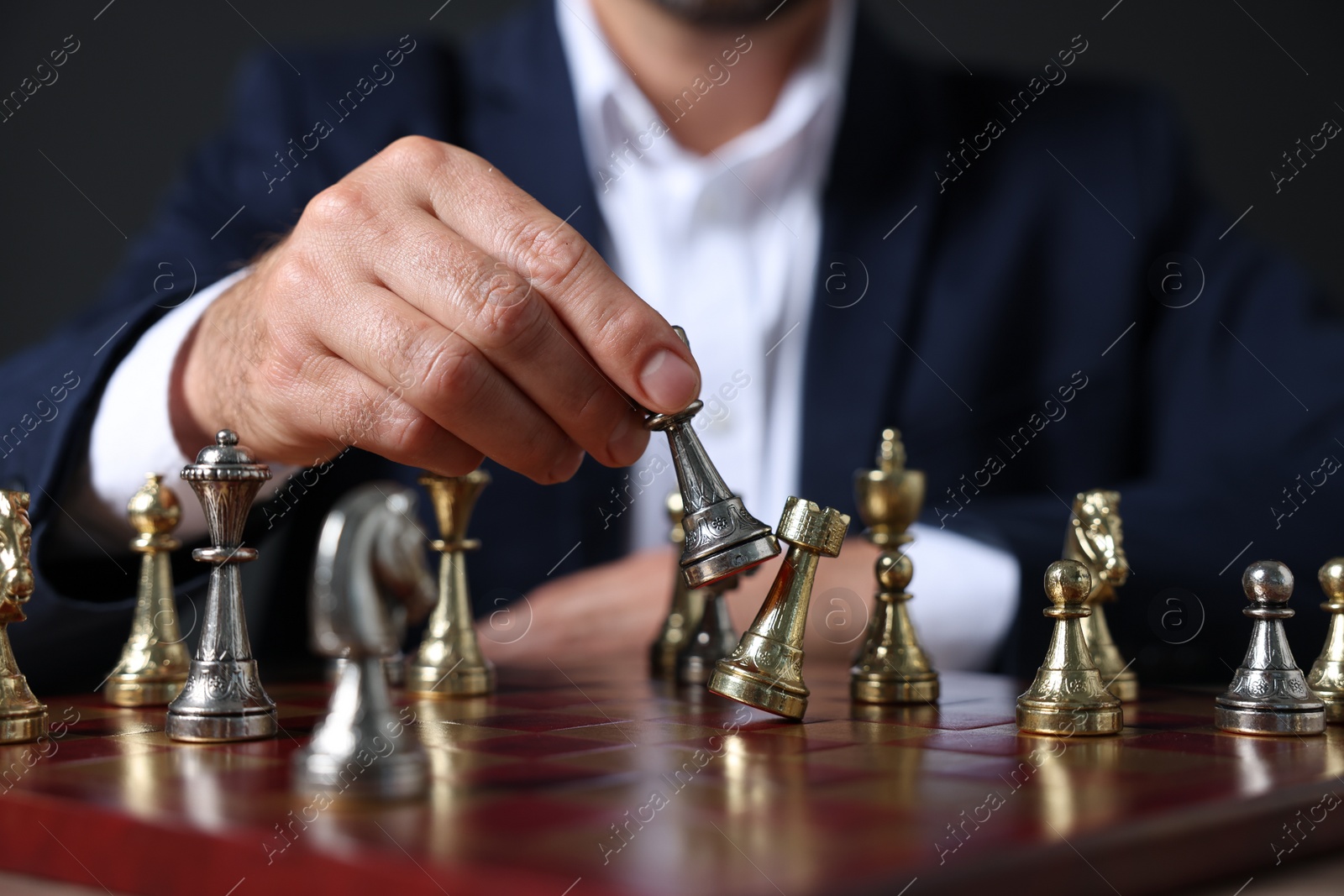 Photo of Man with game piece playing chess at checkerboard against dark background, closeup