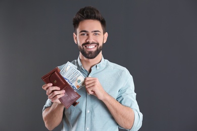Photo of Happy young man with wallet full of money on grey background