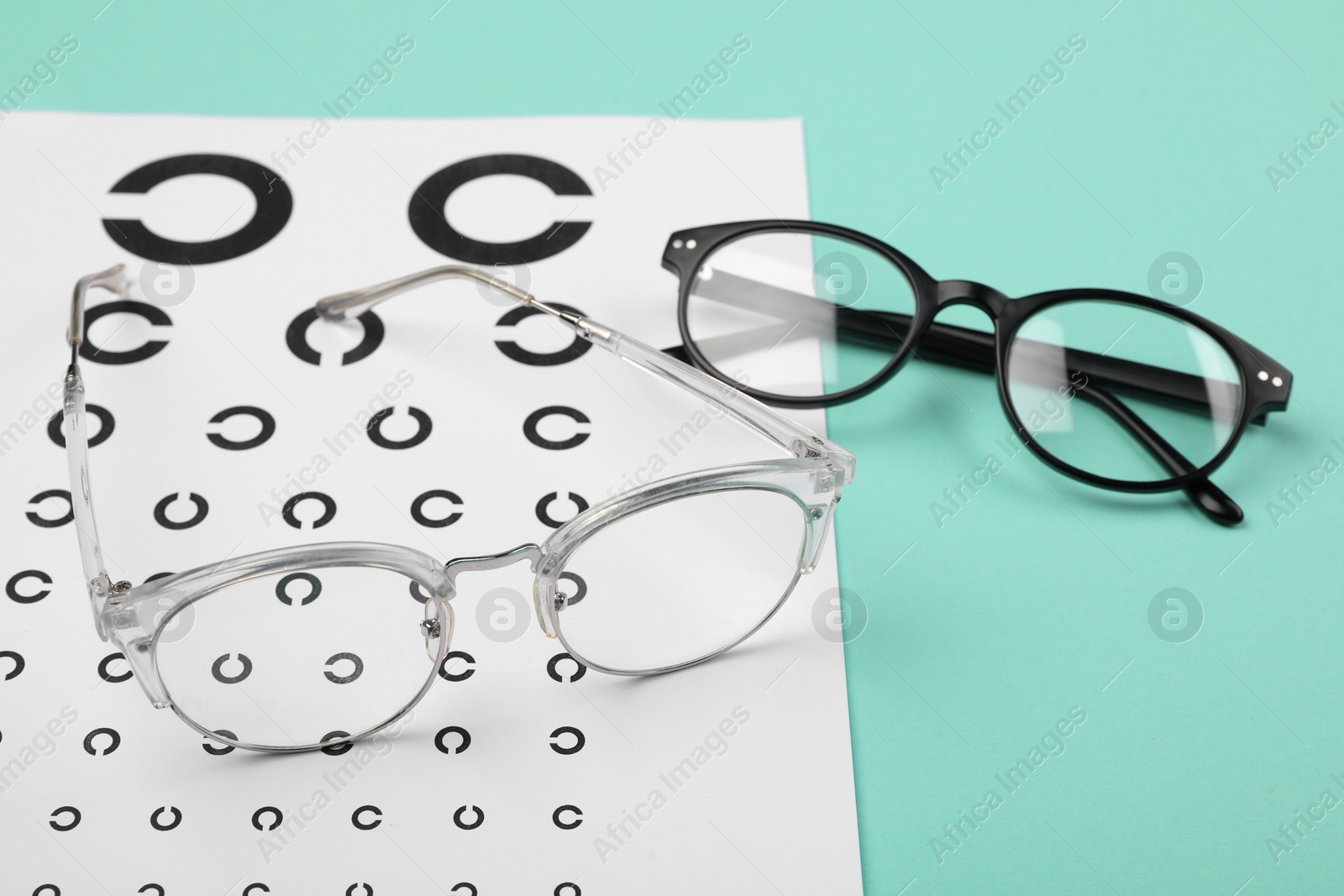 Photo of Vision test chart and glasses on turquoise background, closeup