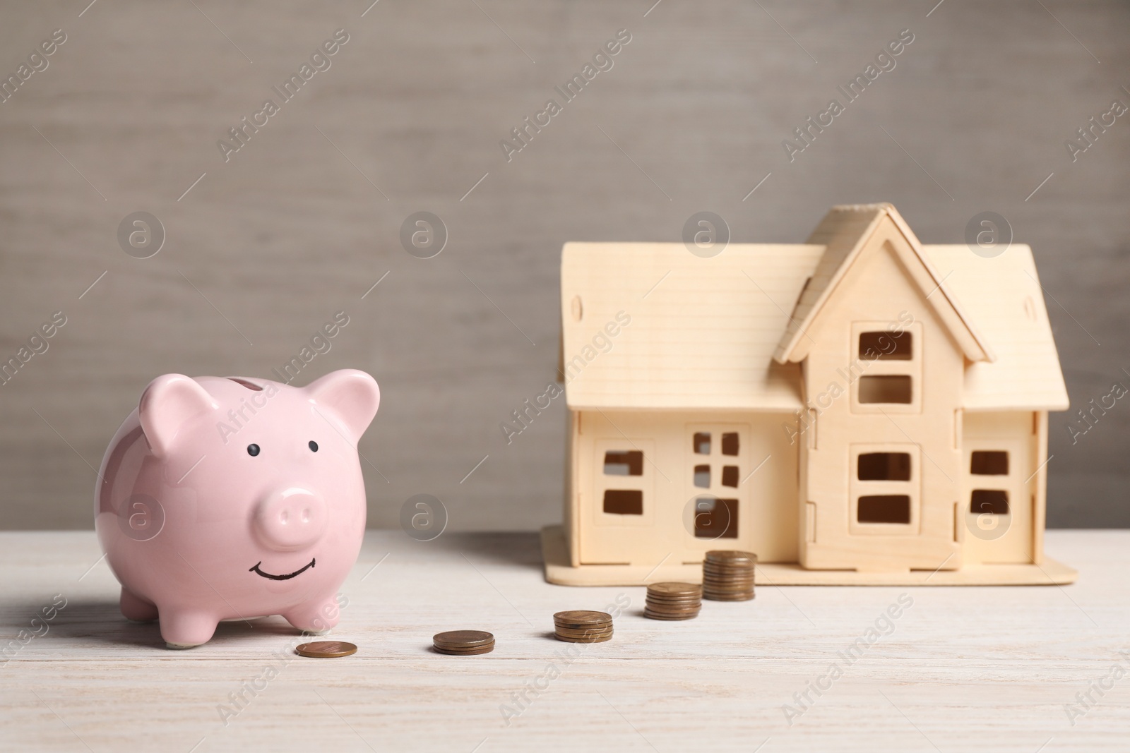 Photo of Piggy bank, little house model and stacks of coins on white wooden table
