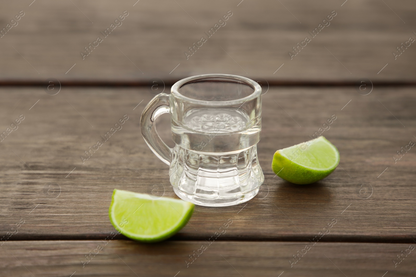 Photo of Mexican tequila shot with lime slices on wooden table, closeup. Drink made from agave