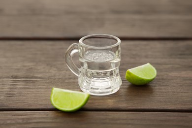 Photo of Mexican tequila shot with lime slices on wooden table, closeup. Drink made from agave