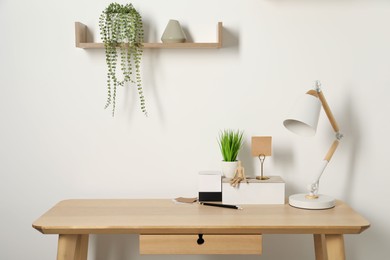 Comfortable workplace with wooden desk near white wall