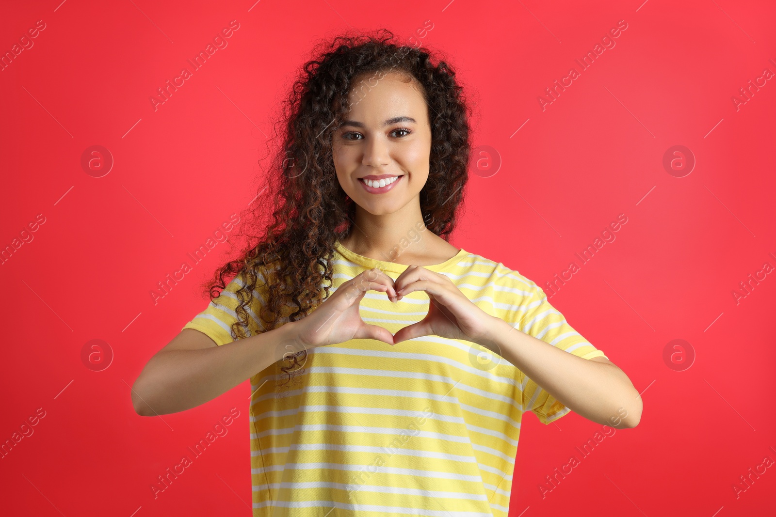 Photo of Happy young African-American woman making heart with hands on red background