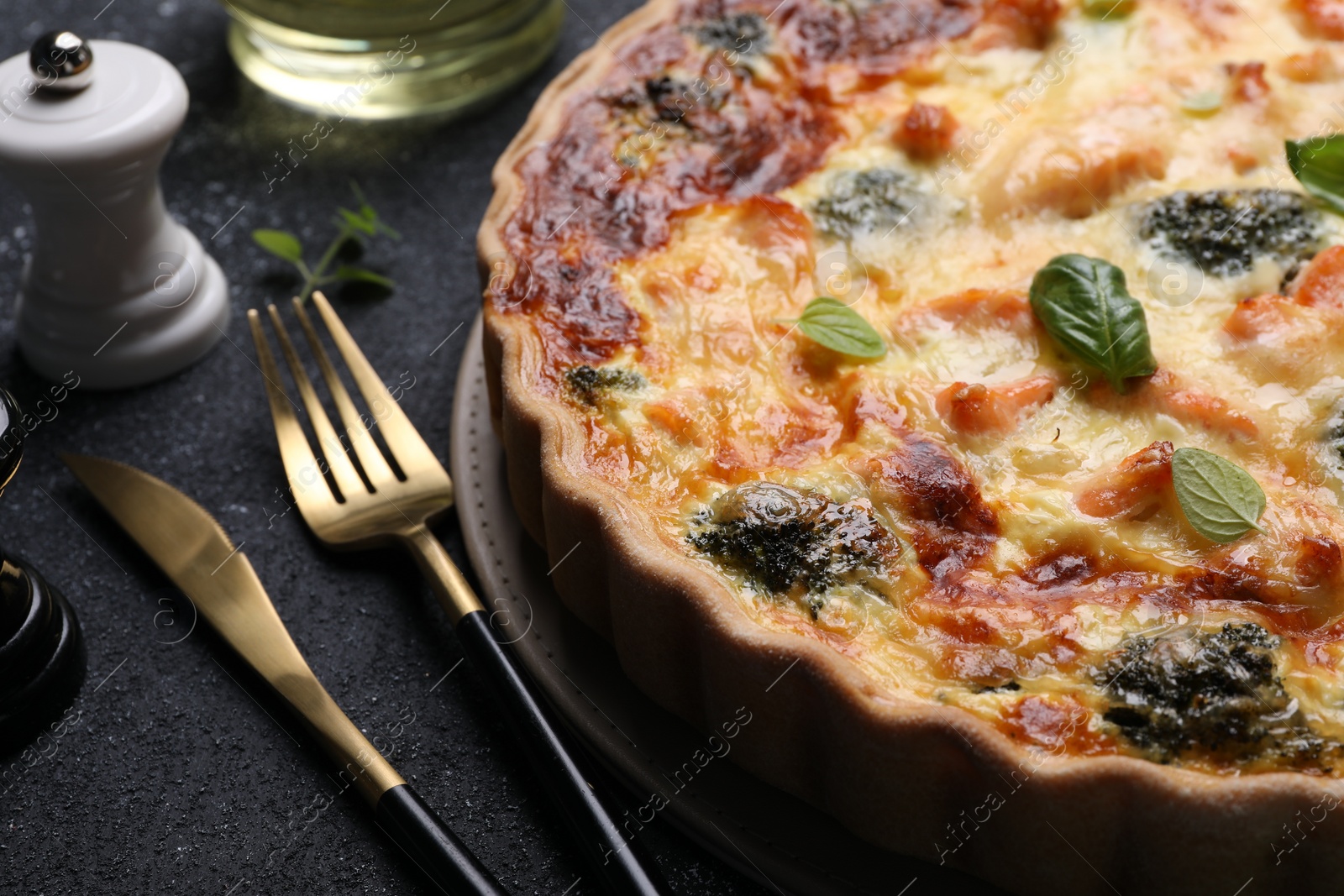 Photo of Delicious homemade salmon quiche with broccoli and cutlery on black table, closeup