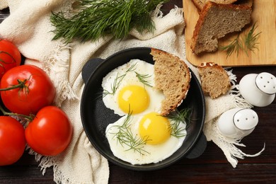 Delicious fried eggs served with bread and tomatoes on wooden table, flat lay