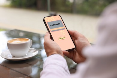 Image of Cashback. Man holding smartphone at table indoors, closeup. Illustration of credit card and percent signs on device screen