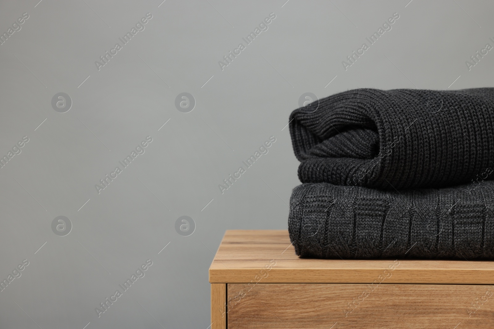 Photo of Stack of knitted sweaters on wooden table against grey background. Space for text