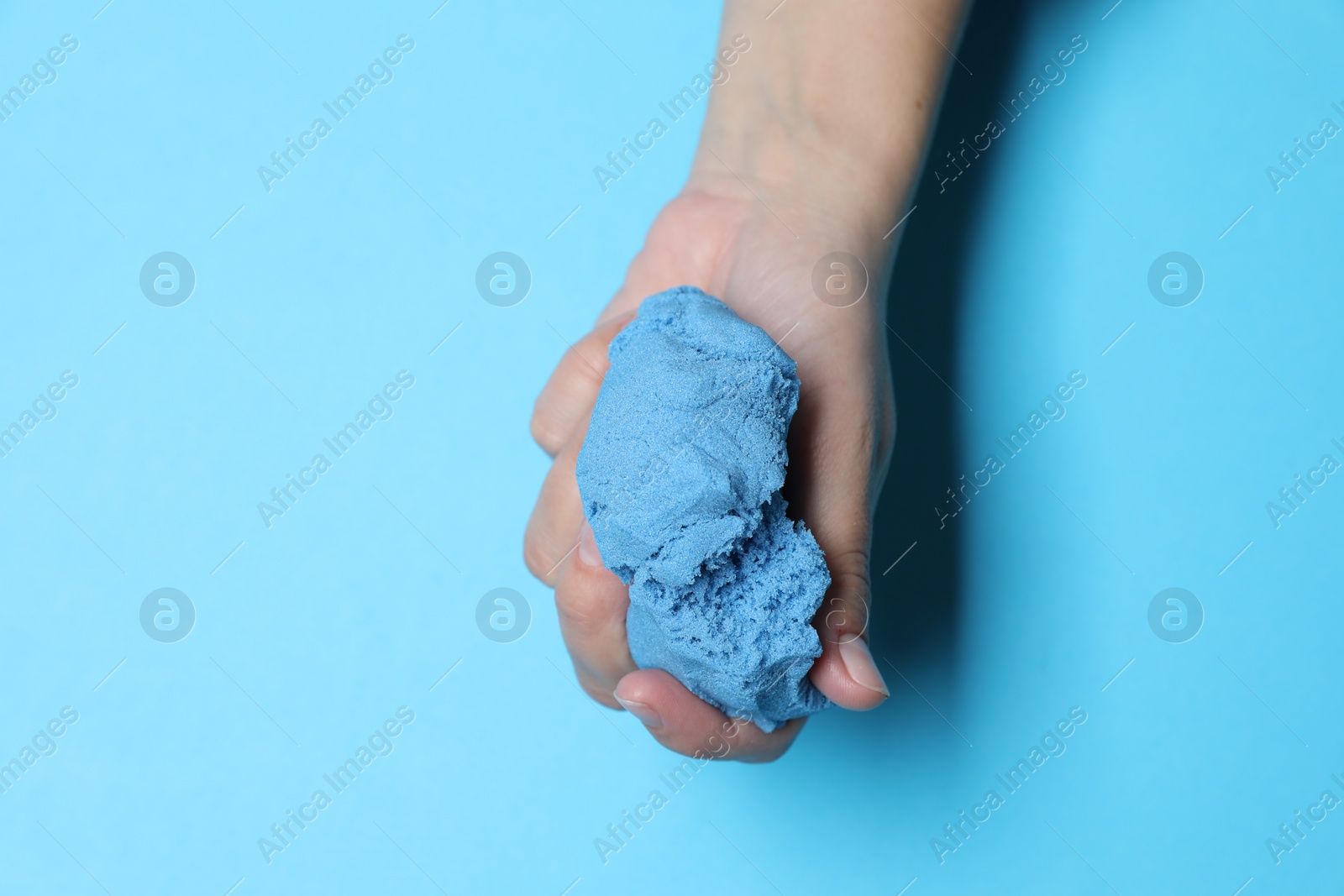 Photo of Woman playing with kinetic sand on light blue background, top view