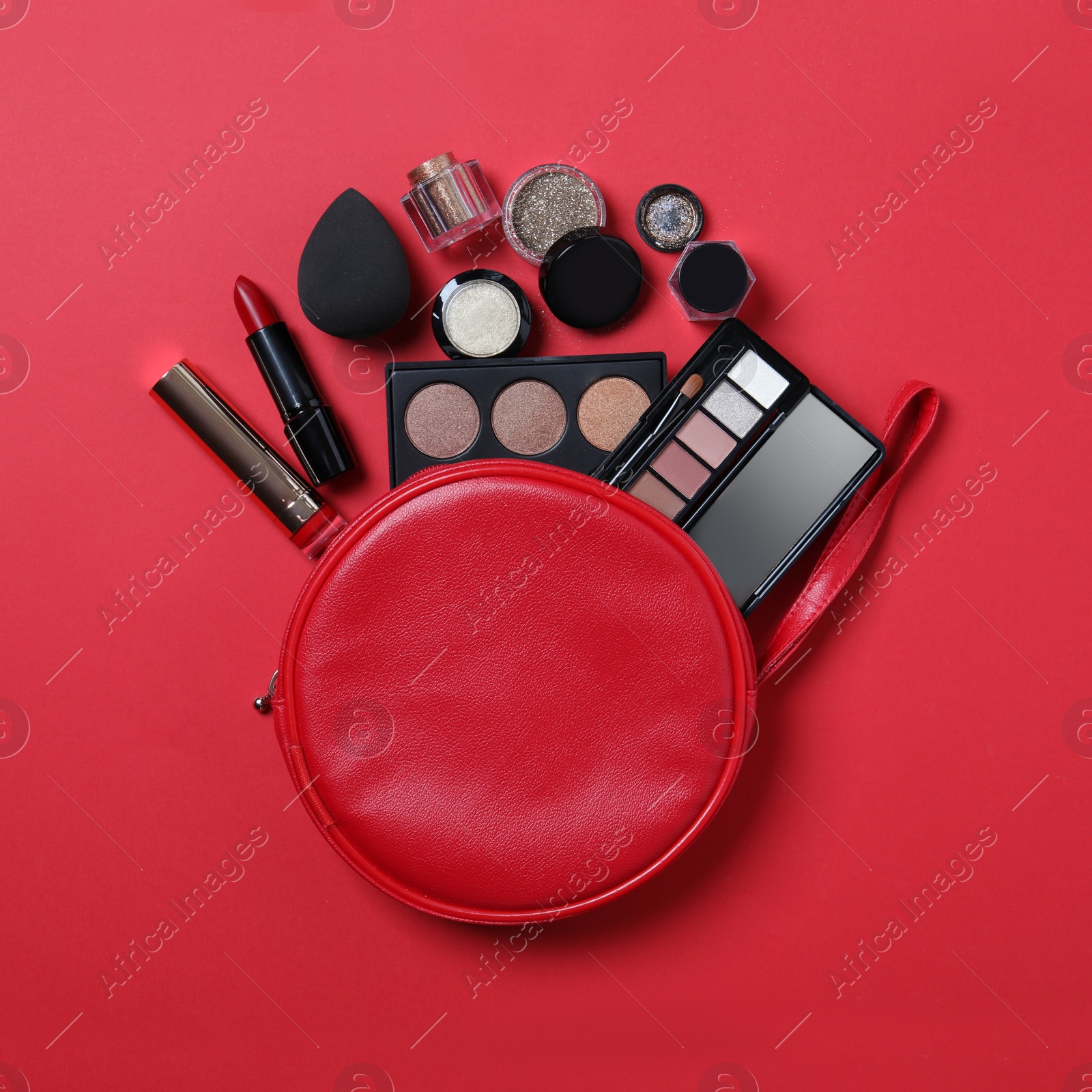 Photo of Cosmetic bag with makeup products on red background, flat lay