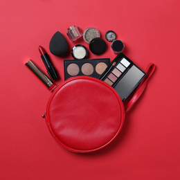 Photo of Cosmetic bag with makeup products on red background, flat lay