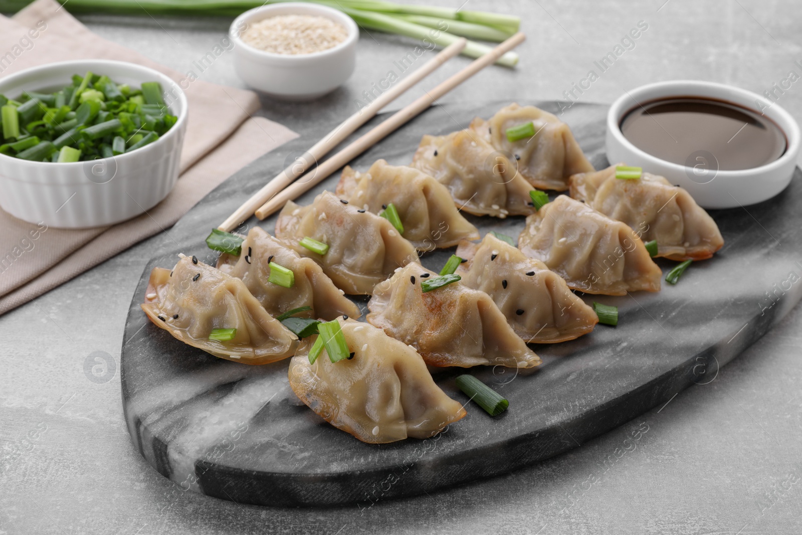 Photo of Delicious gyoza (asian dumplings) with green onions, soy sauce and chopsticks on light gray table